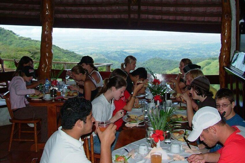 A group of people dining at an outdoor restaurant with a scenic view of hills in the background. 3
