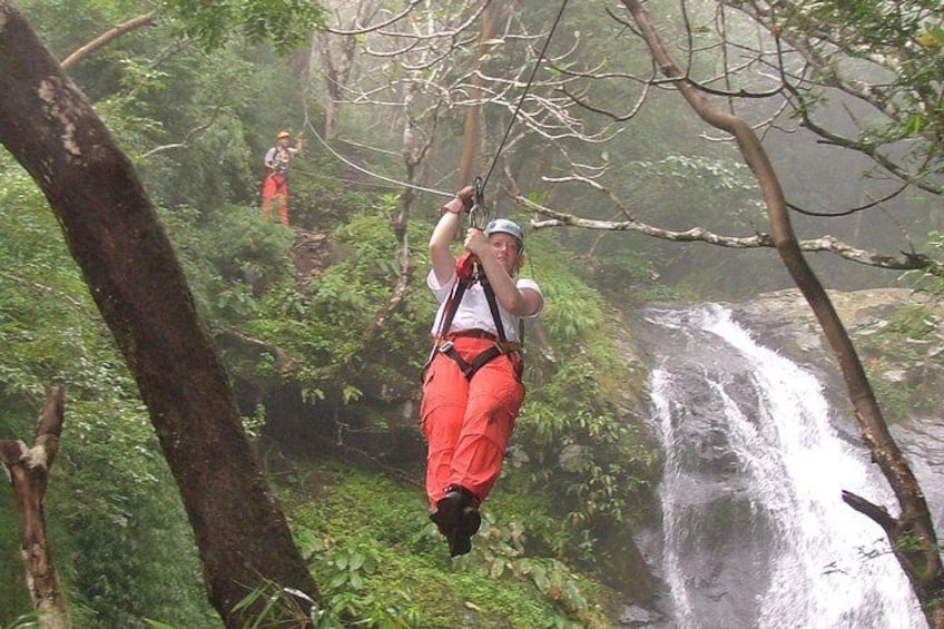 A person zip-lining through a forest with a waterfall in the background. 1