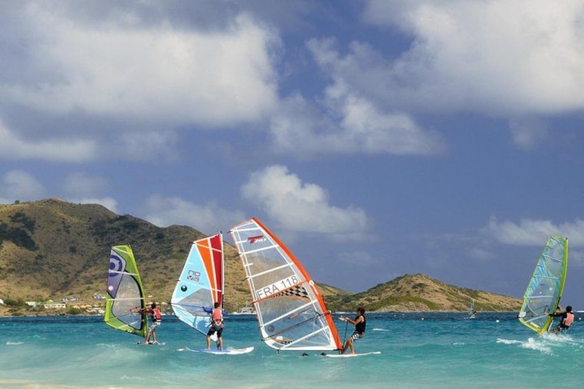 Windsurfers on a beach with mountains in the background. 4