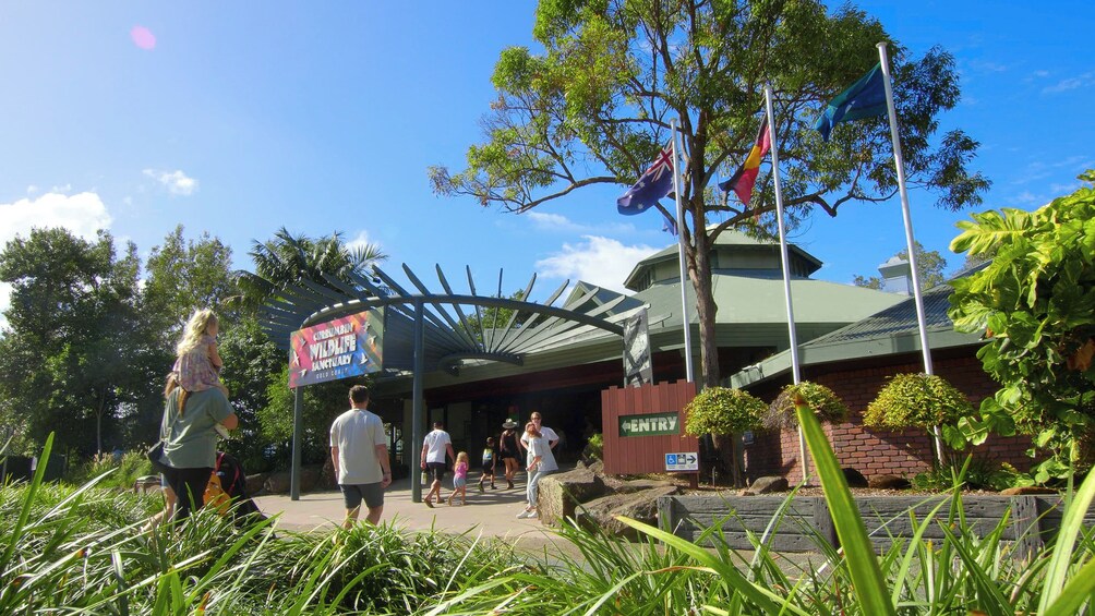 A wildlife sanctuary entrance with a sign, flags, and people walking. 3