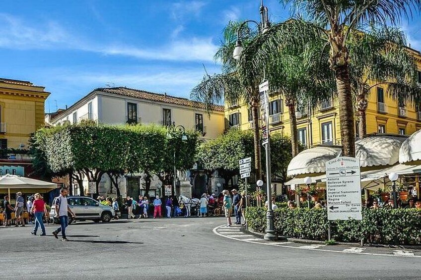 Eine belebte Straße mit Fußgängern, Palmen und Gebäuden mit gelb-weißen Fassaden. 3