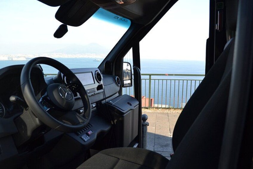 Het interieur van een voertuig, met een stuurwiel, dashboard en uitzicht op de zee door de geopende deur. 3