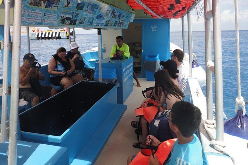 A group of people on a boat with a blue interior, some wearing life jackets, and a person in a neon vest. 2