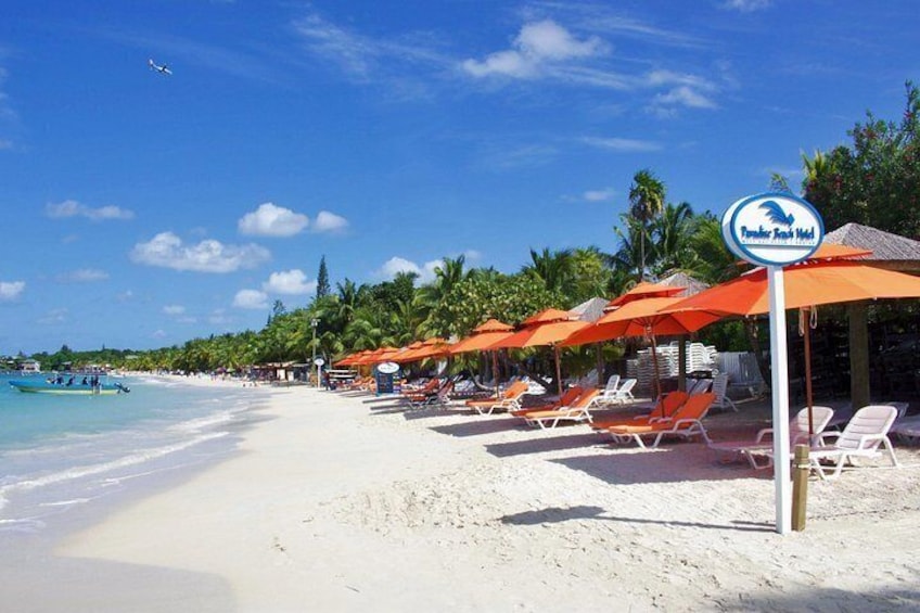 Una playa con arena blanca, sombrillas naranjas y un cartel del Hotel Flamingo Sands. 2