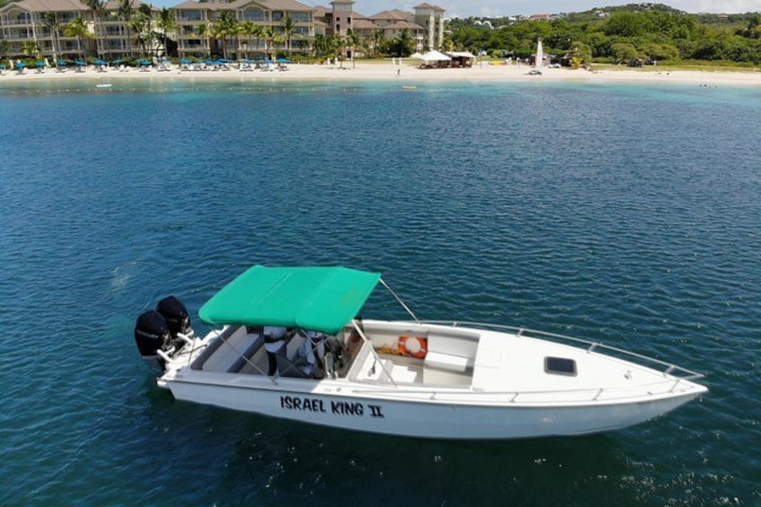 Un barco llamado 'ISRAEL KING II' con un toldo verde, atracado cerca de una playa con palmeras y un hotel al fondo. 1