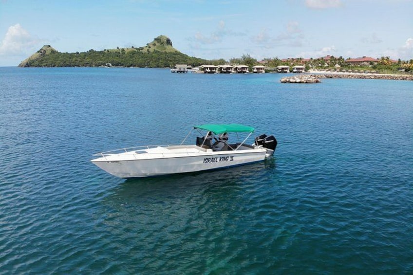 Una lancha rápida blanca con toldo verde en un mar tranquilo, rodeada de agua azul cristalina y una isla distante con edificios. 4