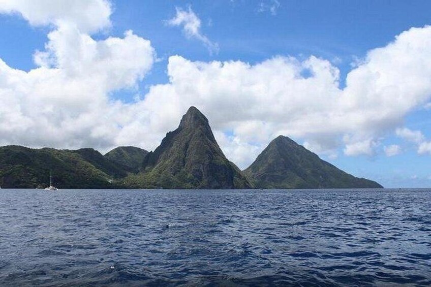 A body of water with a sailboat, surrounded by green hills and a prominent mountain peak under a partly cloudy sky. 2