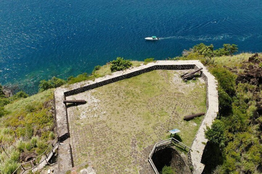 A coastal fortification with cannons, a grassy area, and a boat on the water. 4