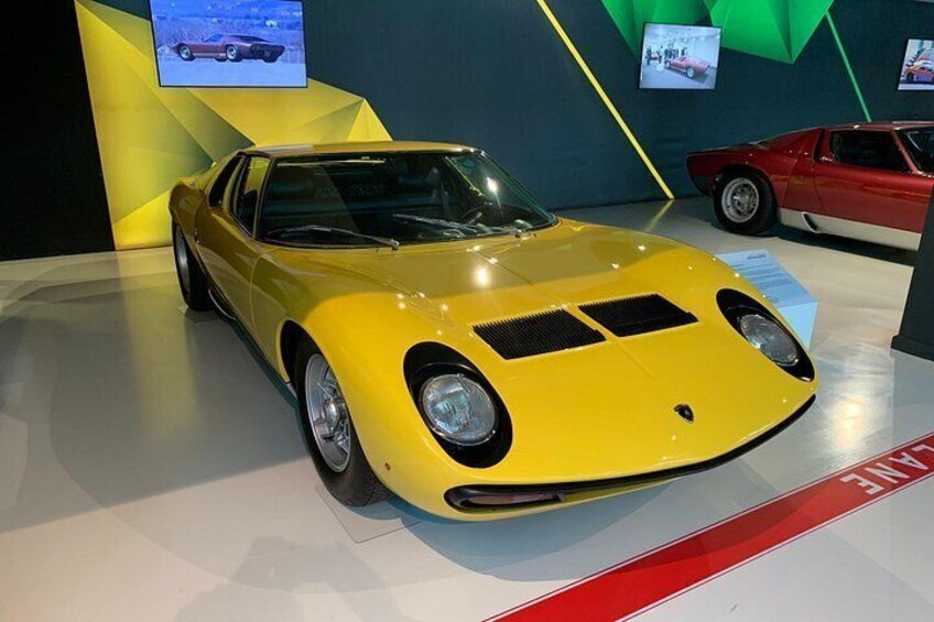 A yellow sports car on display with a red and white car in the background. 5