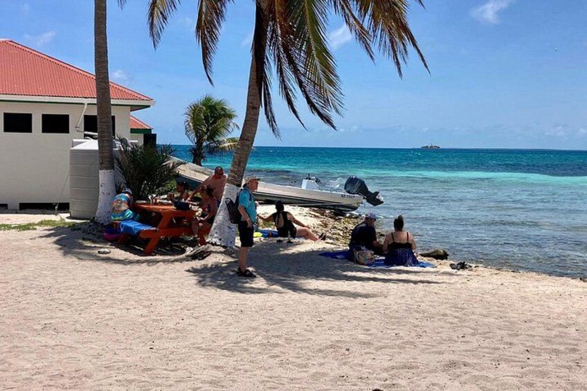 A beach with people relaxing, a boat, and a building with a red roof. 1