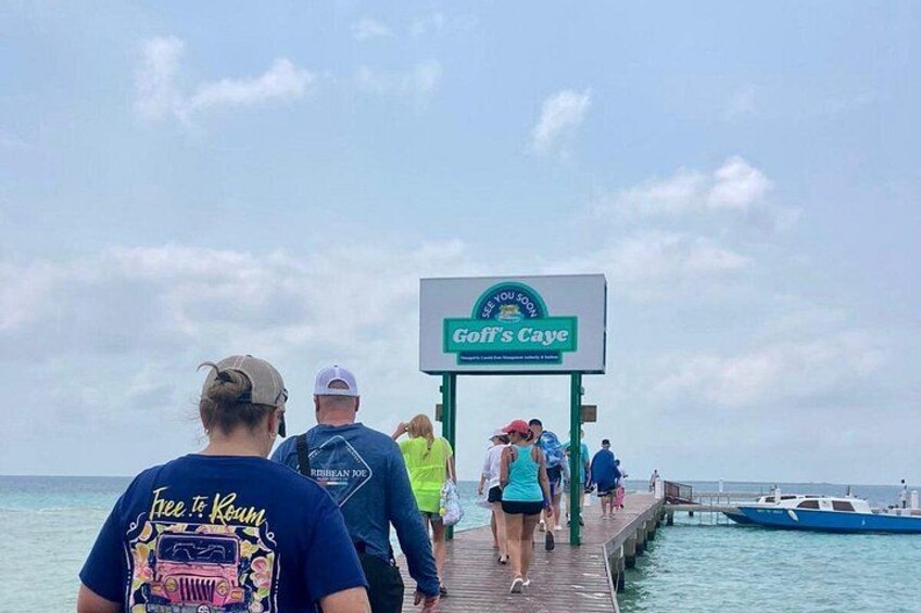 A pier with people walking towards a sign for Goff's Caye. 2