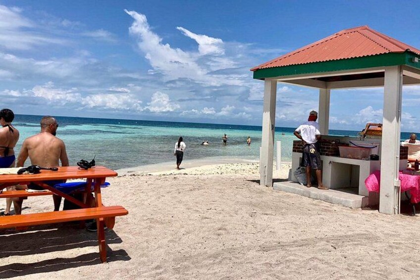 A beach with a gazebo, a man grilling, and people relaxing. 3
