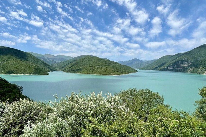 A lake surrounded by green hills under a partly cloudy sky. 1