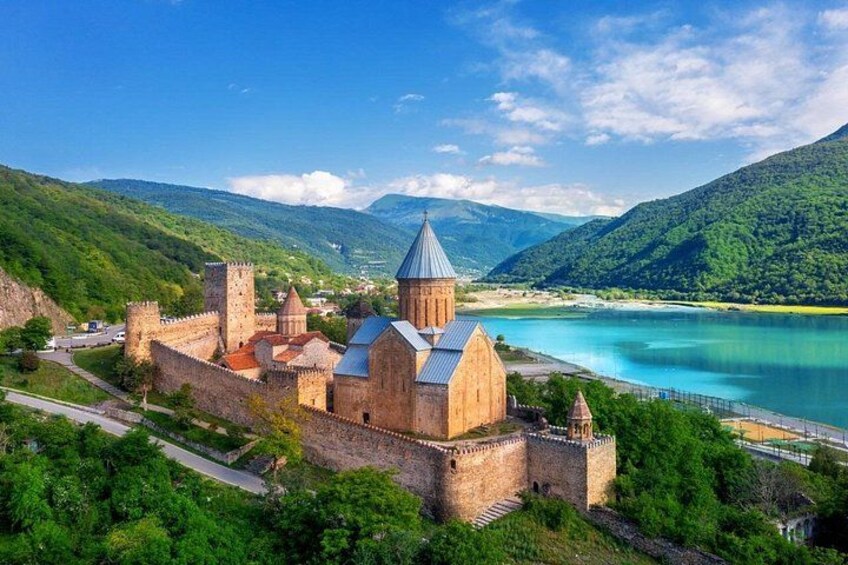 A historic castle with a church, surrounded by lush green hills and a clear blue lake. 4
