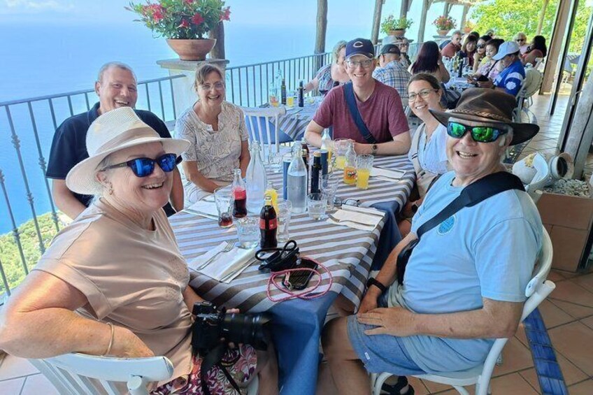 A group of people dining at an outdoor table with a scenic view of the ocean. 5