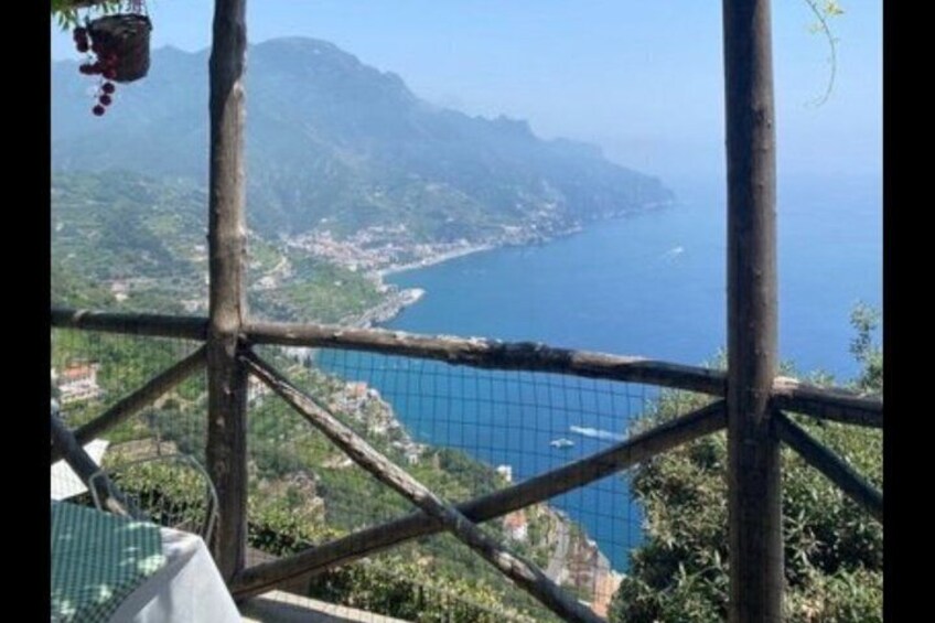 A coastal landscape with a view of the sea and mountains, a wooden fence, and a hanging basket. 1