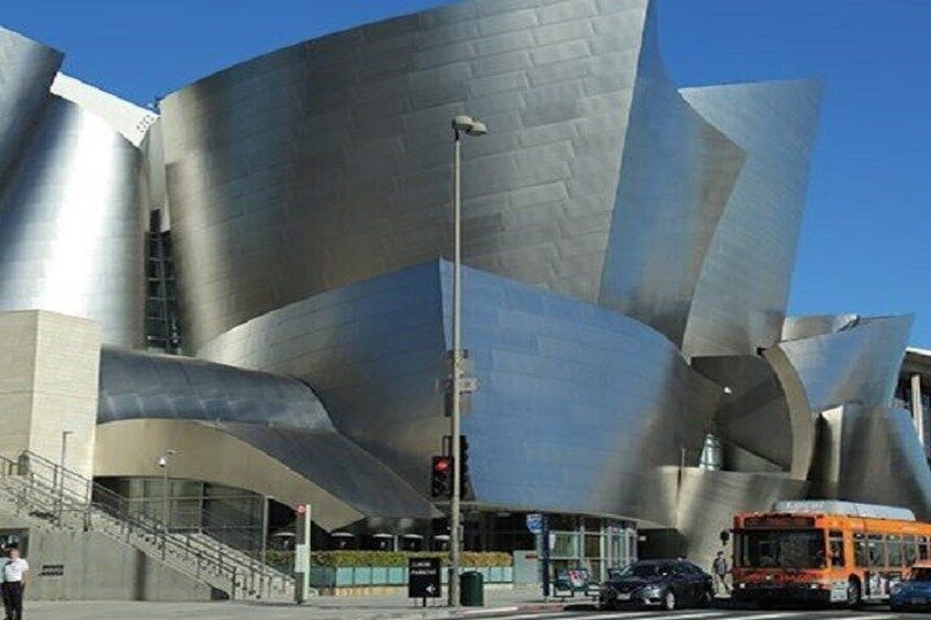 A modern architectural building with curved metallic surfaces and a staircase leading to the entrance. 1
