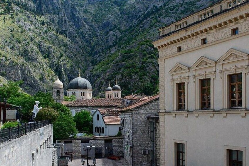 A mountainous landscape with a church featuring domes and a bell tower, surrounded by buildings and a person on a balcony. 3