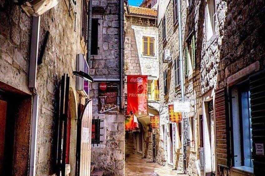 A narrow street with stone buildings, a pizza shop, and a red Coca-Cola sign. 2