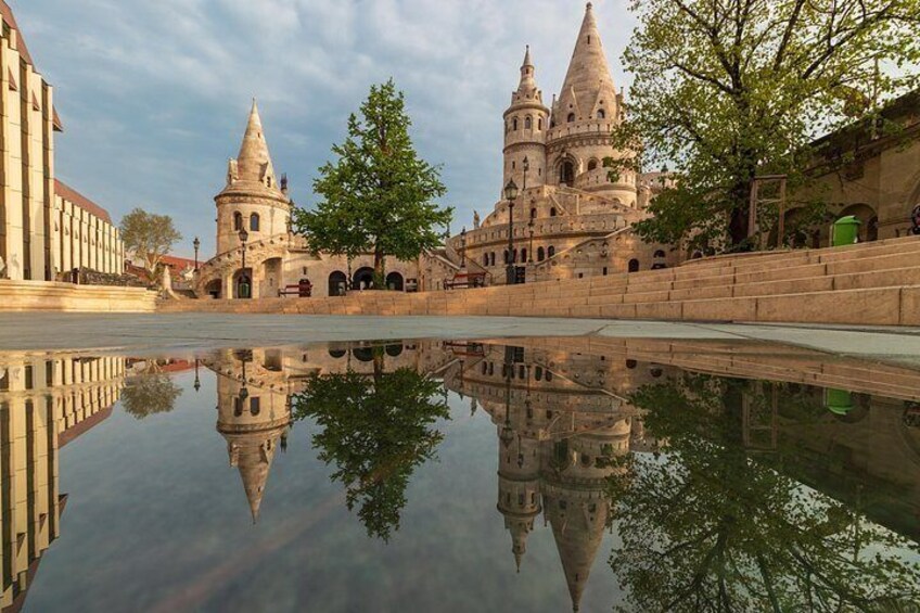 Un edificio histórico con su reflejo en el agua, un árbol y un cielo despejado. 2