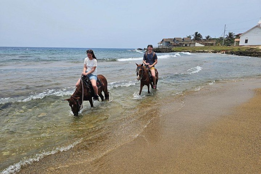 Two people riding horses along a beach with shallow water. 3
