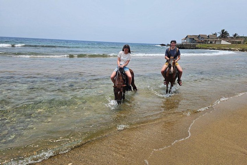 Two people riding horses on a beach near the water. 2