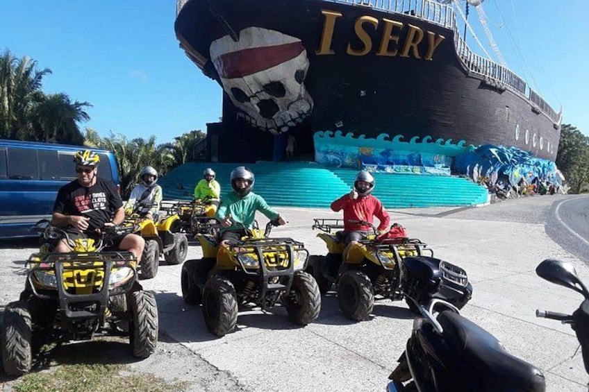 People riding ATVs in front of a large pirate-themed ship. 1