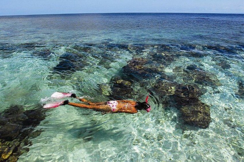 Iemand snorkelt in helderblauw water tussen rotsen. 2