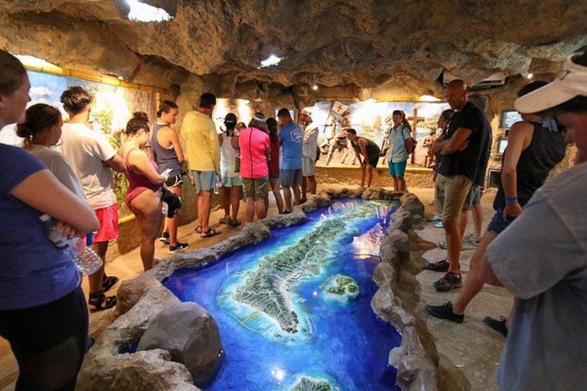 A group of people observing a large, illuminated model of a coastal landscape. 2