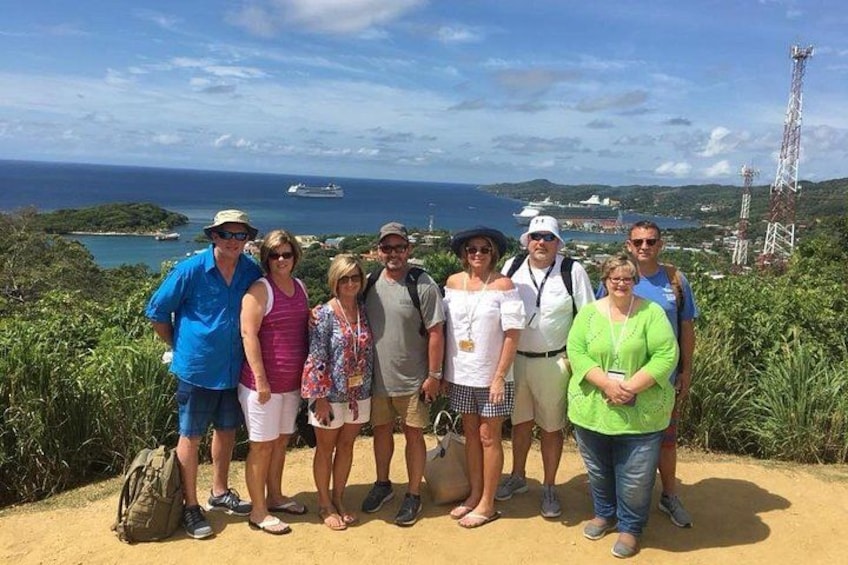 A group of people standing on a dirt path with a view of the ocean and a cruise ship in the distance. 5