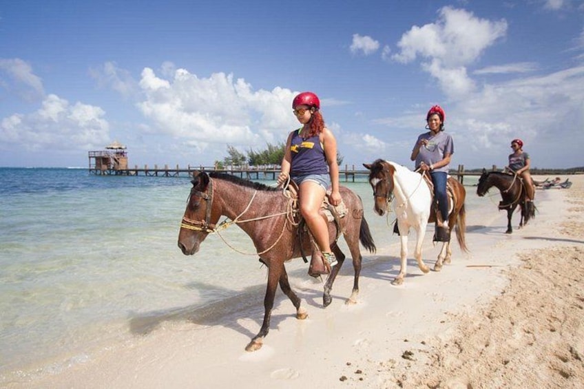 Three people riding horses on a beach with a pier in the background. 3