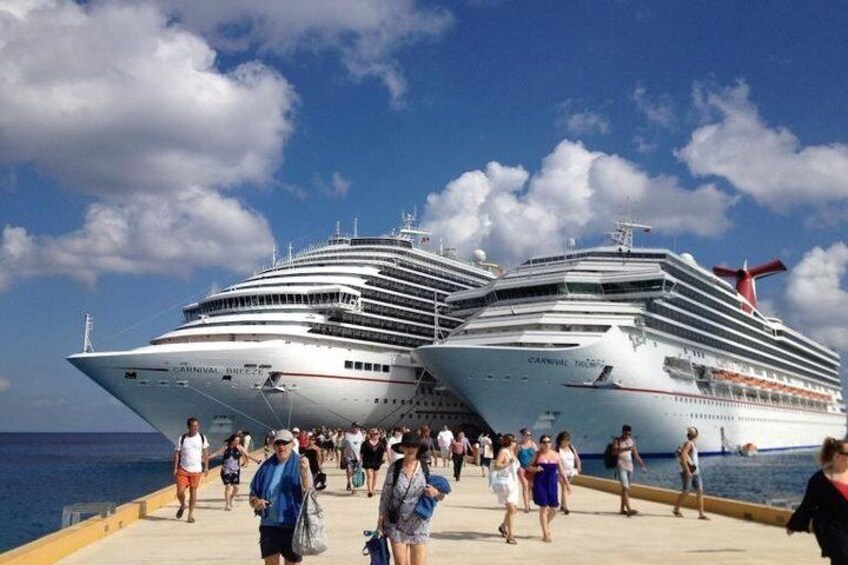 Two cruise ships docked at a port with people walking on the pier. 3