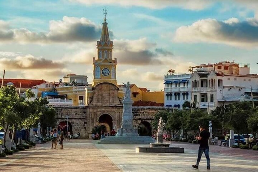 A historic square with a prominent clock tower, a statue, and surrounding buildings. 5