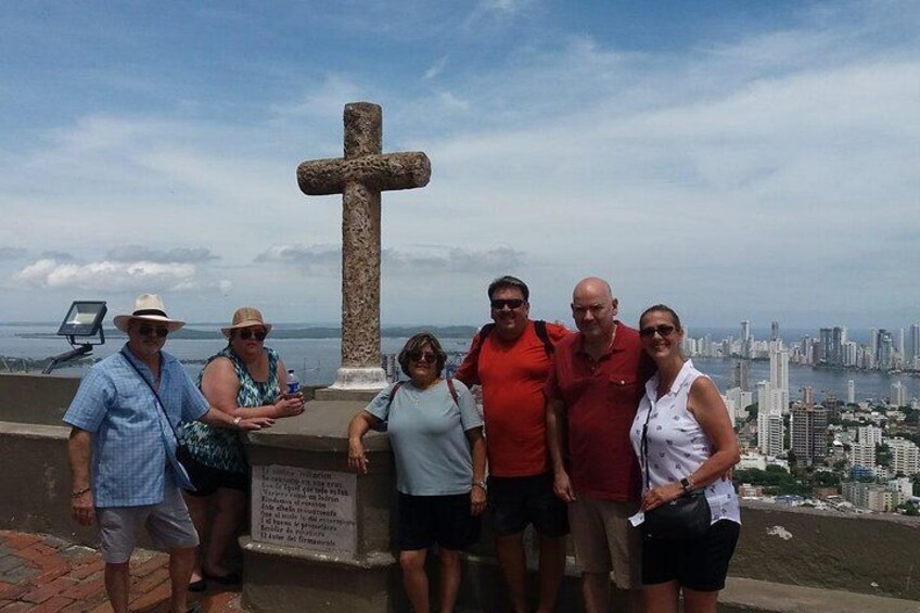 A group of people standing in front of a large stone cross with a cityscape in the background. 1