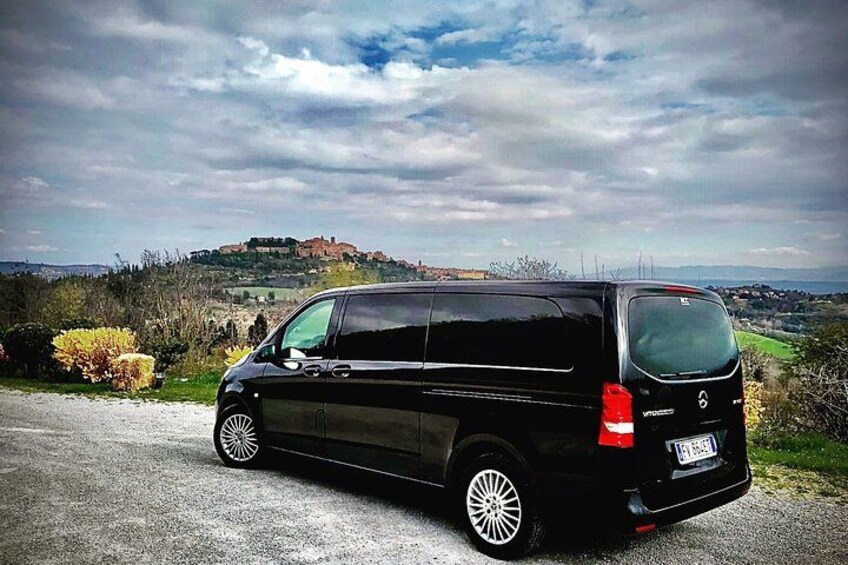 A black van parked on a gravel road with a scenic view of a hill and a castle in the background. 2