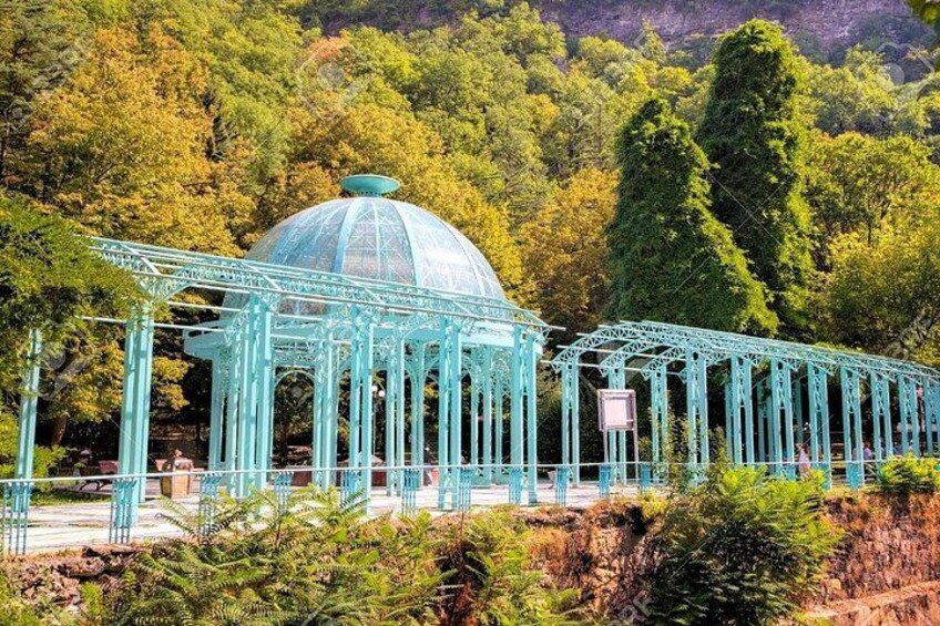Une serre aux murs de verre turquoise, surmontée d’un dôme, et entourée d’une végétation luxuriante et d’arbres. 4