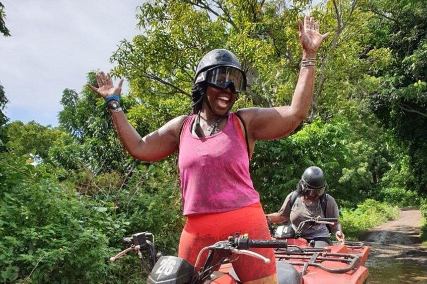 A person in a pink tank top and red shorts on a red ATV, with another person in the background. 2