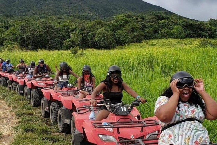 Un groupe de personnes sur des quads rouges se trouve dans un champ herbeux, avec une montagne en arrière-plan. 2