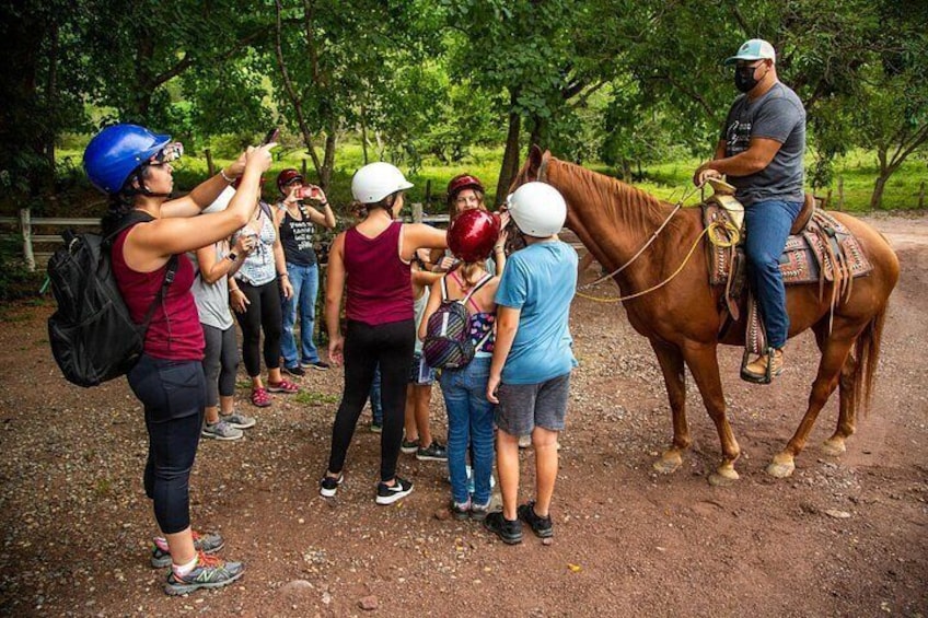 Un gruppo di persone su un sentiero sterrato, alcune con caschi, e una persona a cavallo. 3