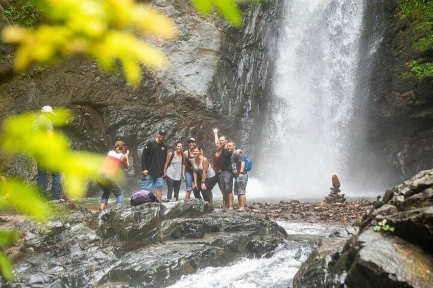 Un gruppo di persone in piedi su rocce vicino a una cascata in una zona boschiva. 2