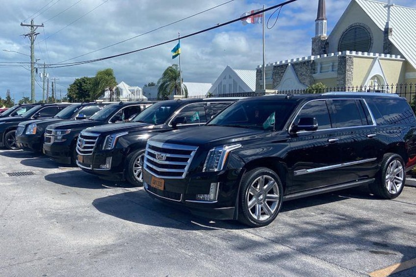 En rad svarta Cadillac-terrängbilar står parkerade på en parkeringsplats med en kyrka och en flagga i bakgrunden. 1