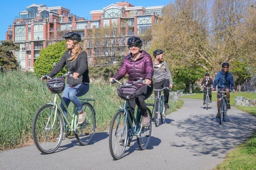 Des personnes font du vélo sur une piste pavée bordée de gazon, avec un ensemble de bâtiments en arrière-plan et des arbres aux feuilles d'automne. 4
