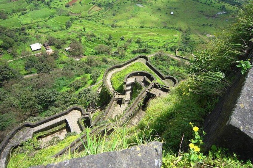 A historical fortification with a winding wall, lush green fields, and scattered buildings in the background. 1