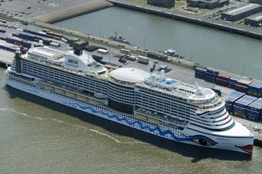 Ein großes Kreuzfahrtschiff liegt an einem Hafen. Es hat mehrere Decks und eine auffällige blaue und weiße Farbgebung. 5