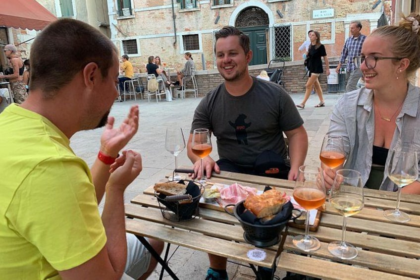 People dining at an outdoor table with food and drinks. 1