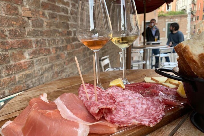 Una tabla de madera con varios embutidos, dos copas de vino y una hogaza de pan sobre una mesa. 2