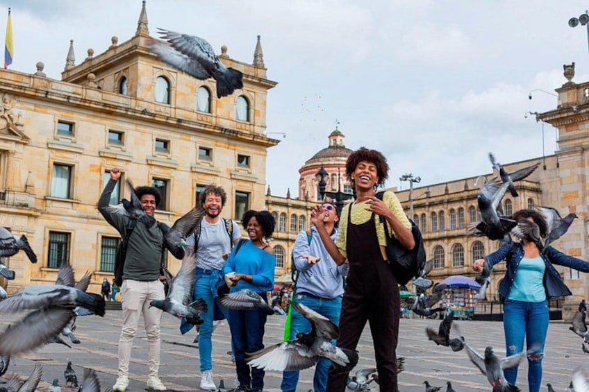 A group of people feeding pigeons in a plaza with historic architecture in the background. 2