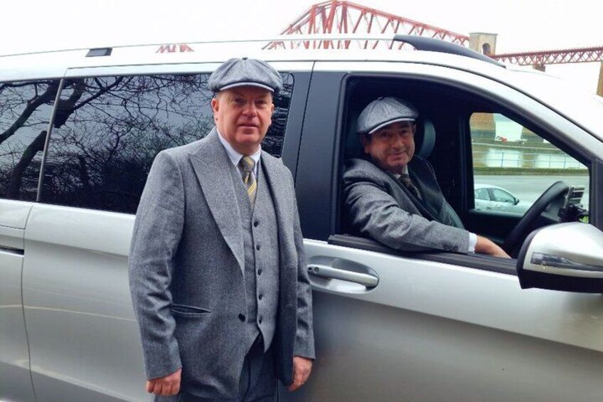 Two men in suits standing next to a silver car. 3