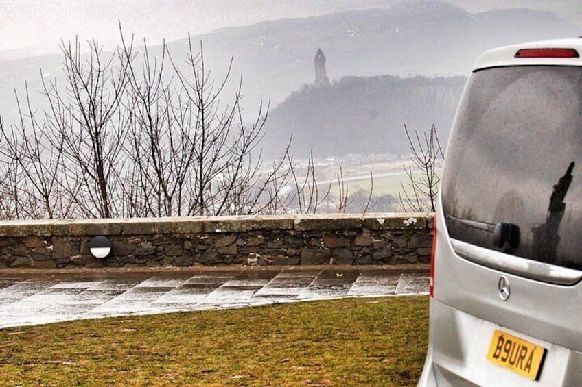 Un'auto parcheggiata su un prato, con un muro di pietra e alberi spogli sullo sfondo. 2