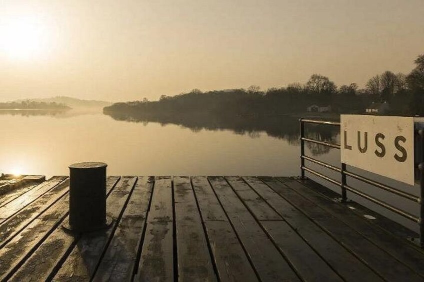 A wooden dock with a sign reading 'LUSS' overlooking a calm lake at sunrise. 4